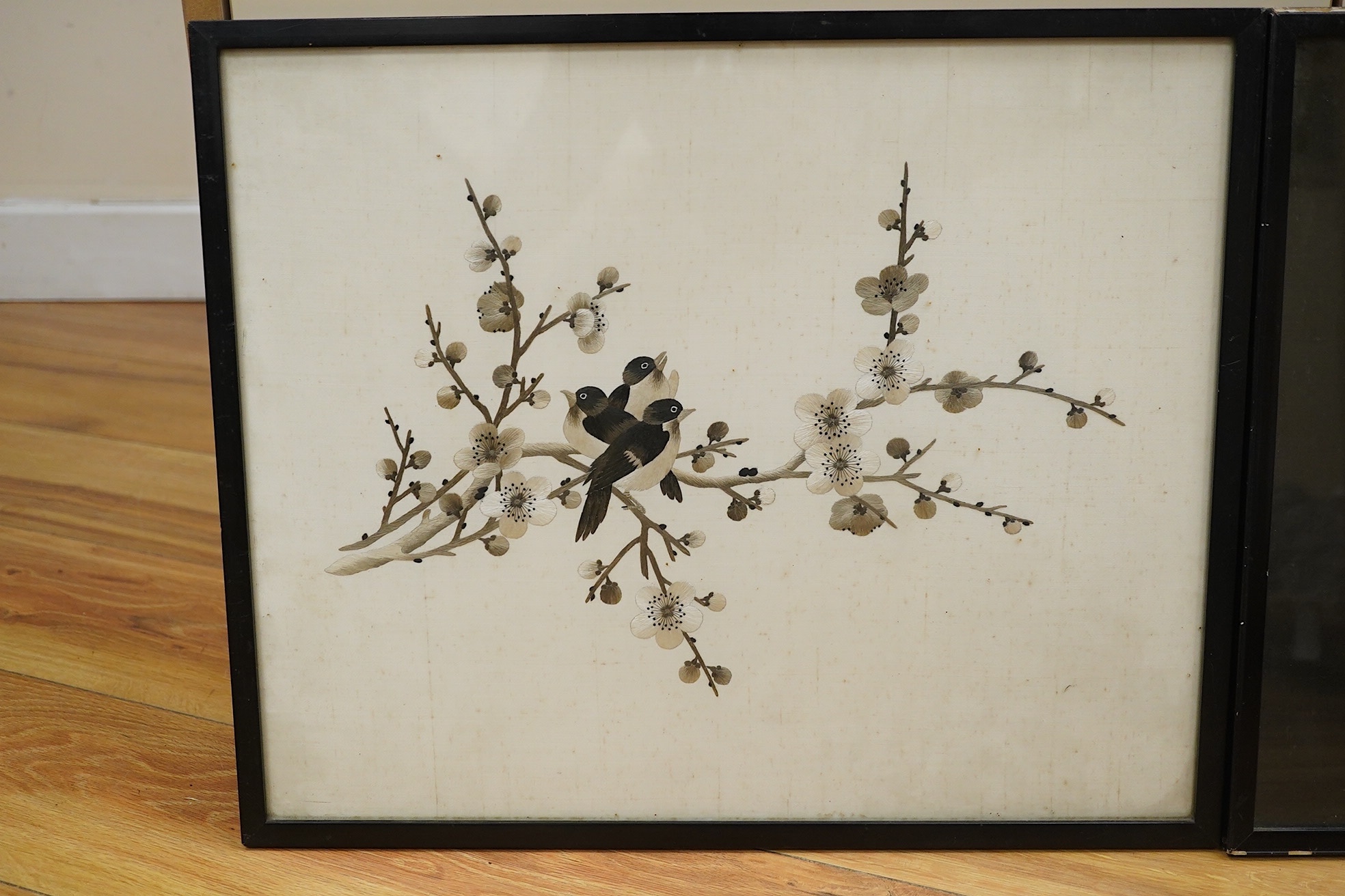 Two Chinese polychromed silk embroidered panels, early 20th century, one on a black silk ground of birds and flowers, the other on a red background of flowers and a monochrome silk embroidered panel of birds and flowers,